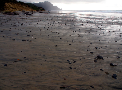 [A skim of water covers the sand as also do many small stones. Clearing rain clouds allow a skim of light from the horizon across the sand.]